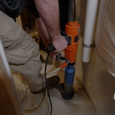 Green Earth Remediation technician actively drilling to install a radon mitigation system in a commercial setting.