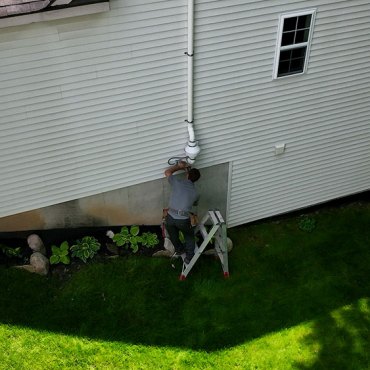 Technician from Green Earth Remediation installing a radon mitigation pipe at a residential property.