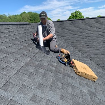 Green Earth Remediation technician securing a radon mitigation pipe on a home's roof, ensuring optimal radon venting.