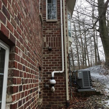 Exterior radon mitigation pipe installation by Green Earth Remediation on a brick residential building.