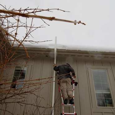 Green Earth Remediation technician installing a radon mitigation system on the roof of a residential building.