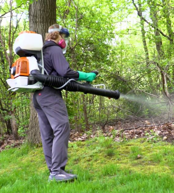 Green Earth Remediation pest control technician applying insecticide outdoors.